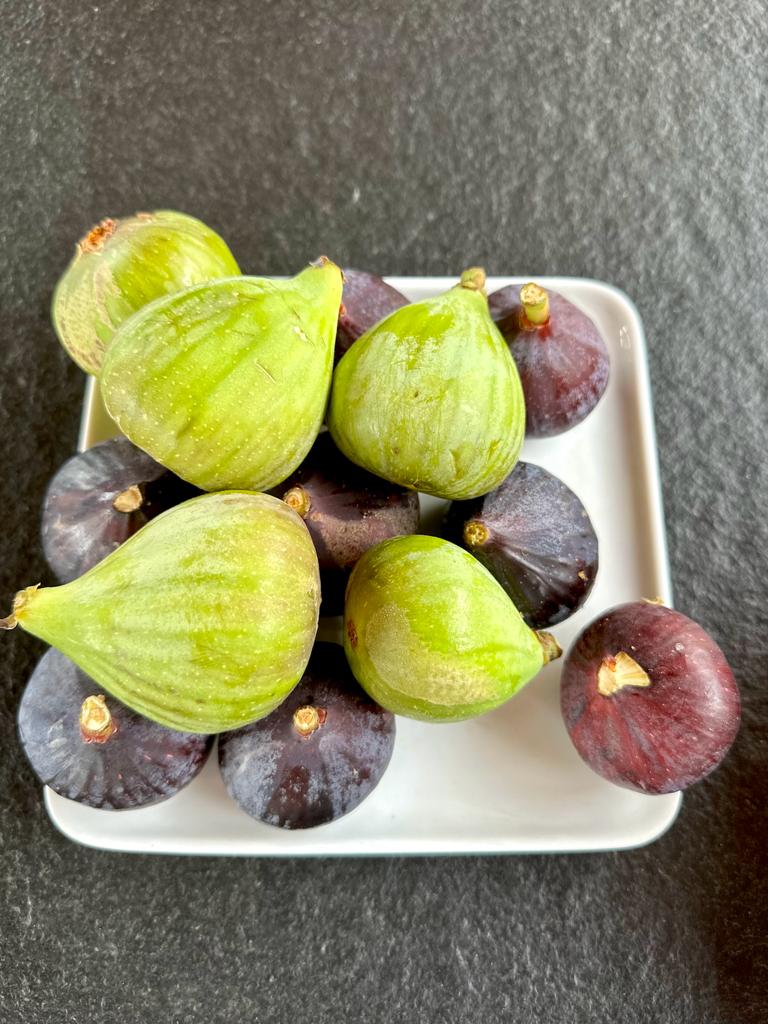 Bowl of fresh figs — green and deep-purple — on a dark surface