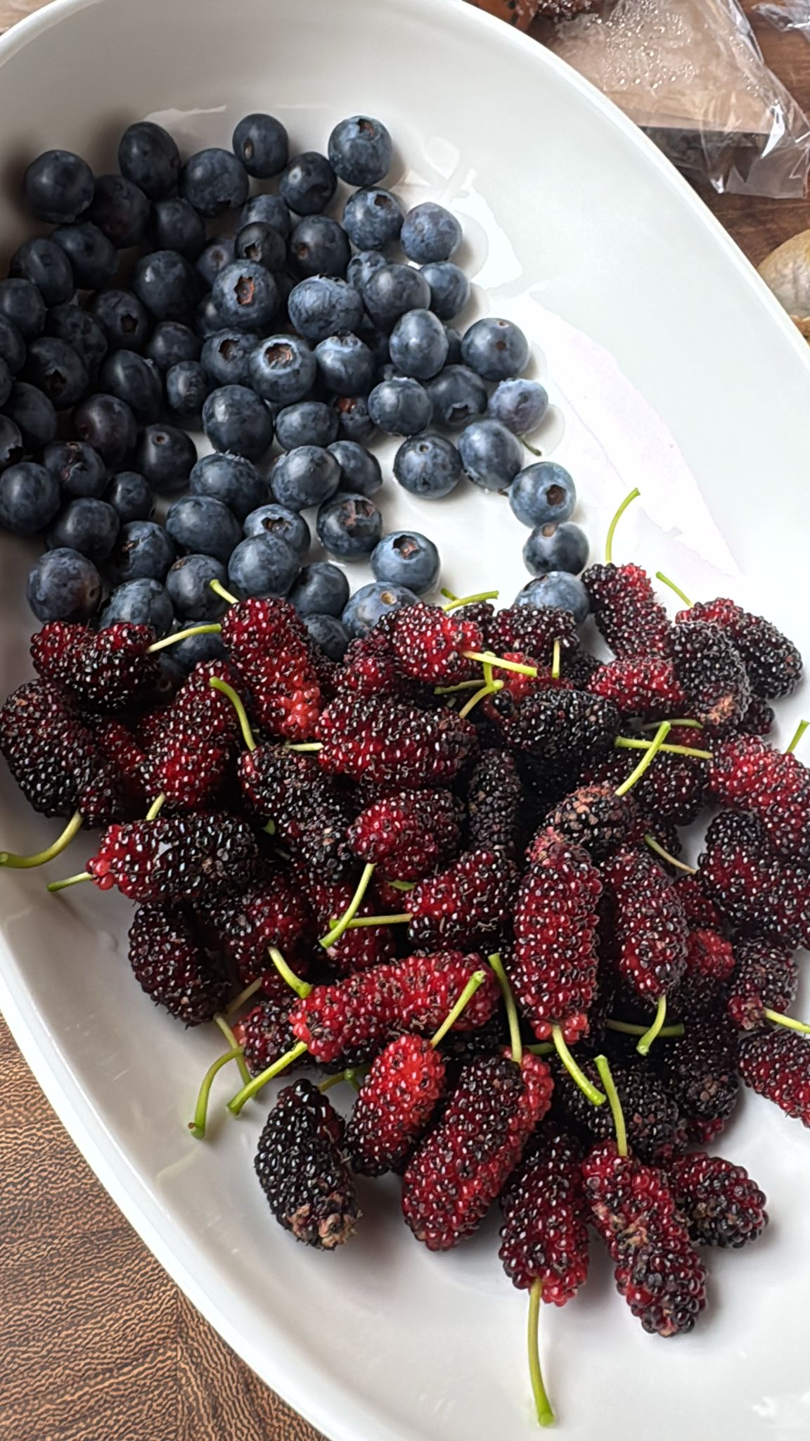 A white oval dish piled with fresh blueberries on one side and ruby-dark mulberries on the other
