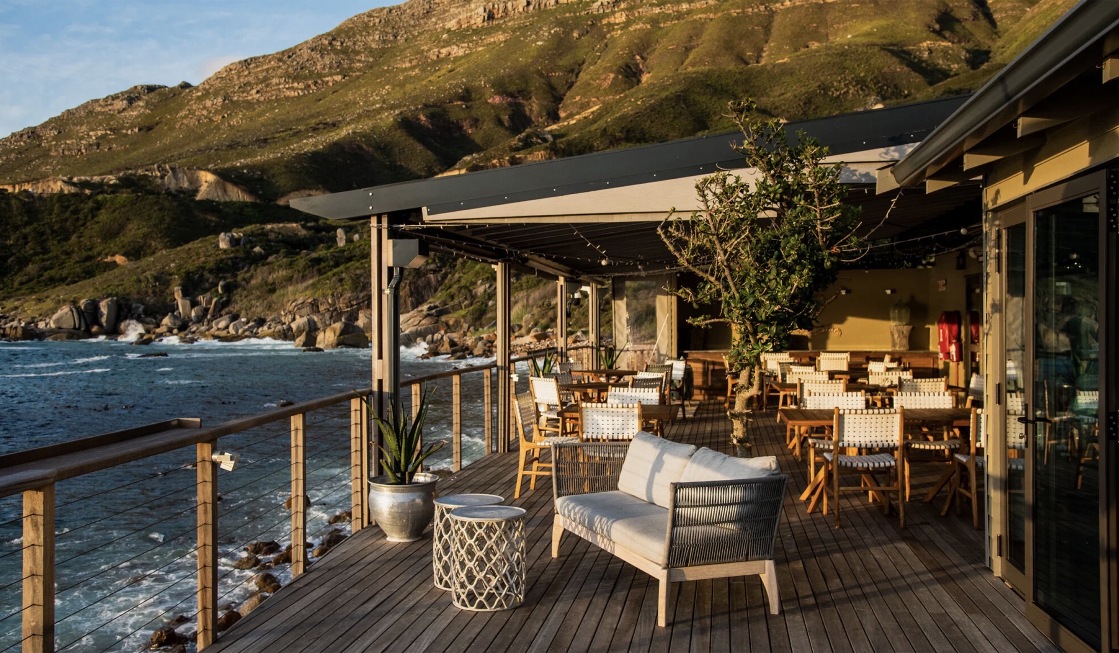 The wooden deck and dining terrace at Tintswalo Atlantic at golden hour, looking out across the Atlantic cove beneath the cliffs of Chapman's Peak