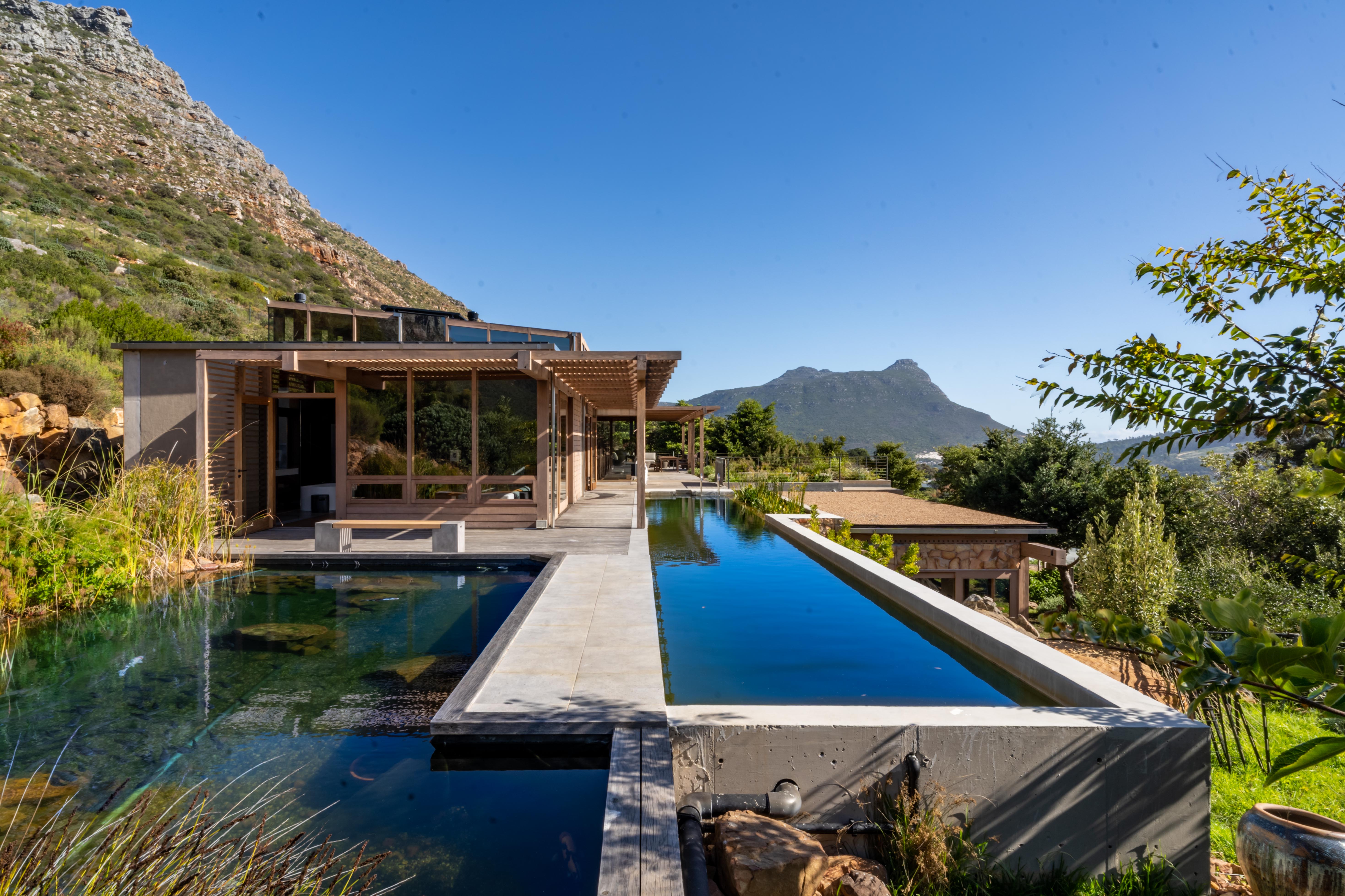 The 20-metre lap pool wrapping around the granite boulder, with the mountain rising directly behind the house